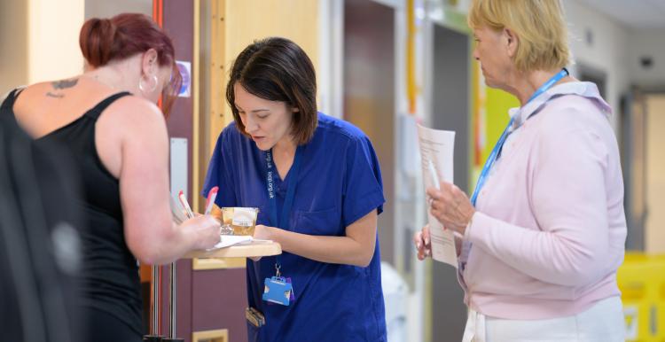 Three women in a hallway filling out a form. Two are clinicians.