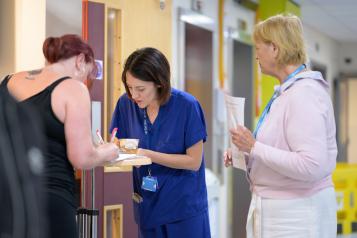 Three women in a hallway filling out a form. Two are clinicians.